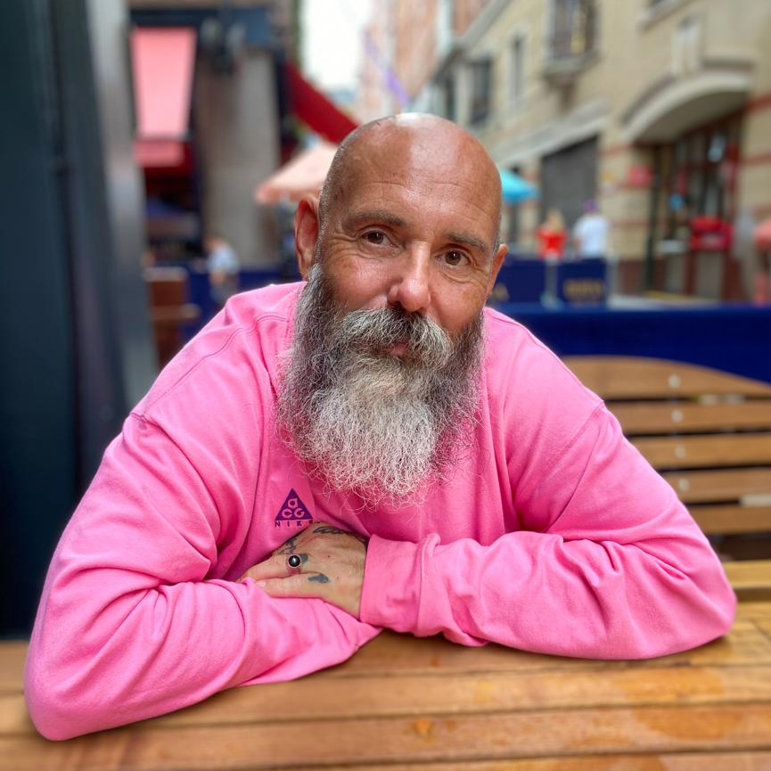Andy sat at a table outside in a pink shirt, smiling.